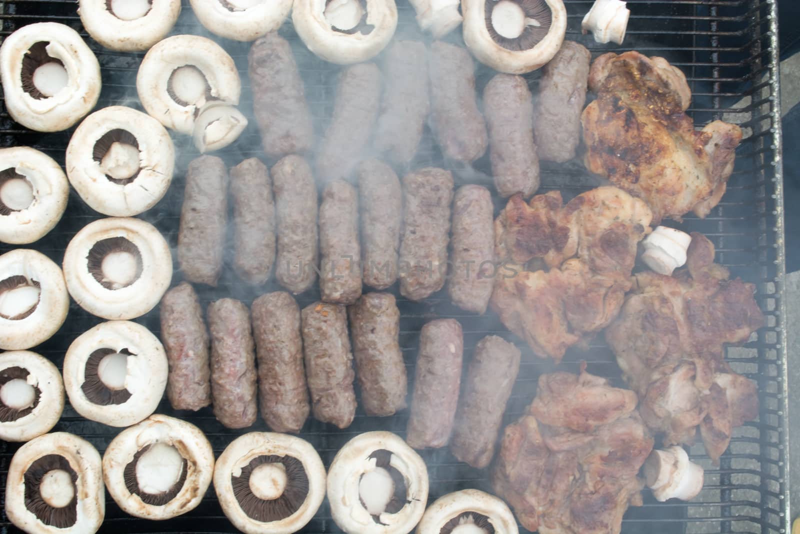 Grilling cevapi and mushrooms. Smoke visible. Upper angle