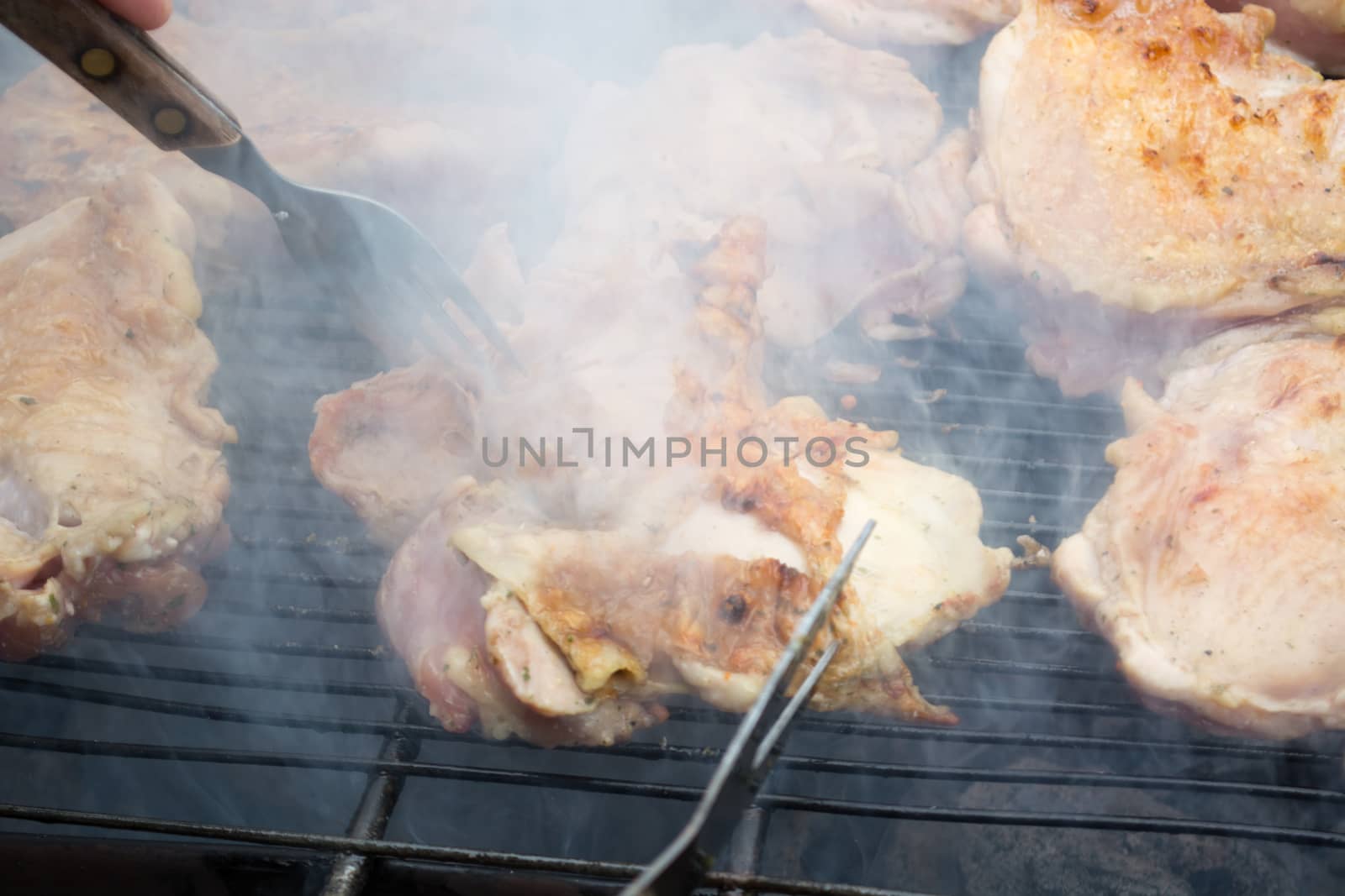 Turning over raw pork chops on grill. Smoke rising from heated grill