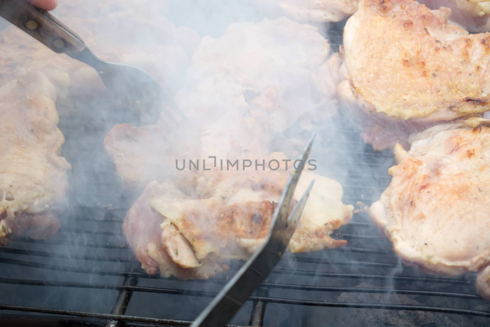 Turning over raw pork chops on grill. Smoke rising from heated grill