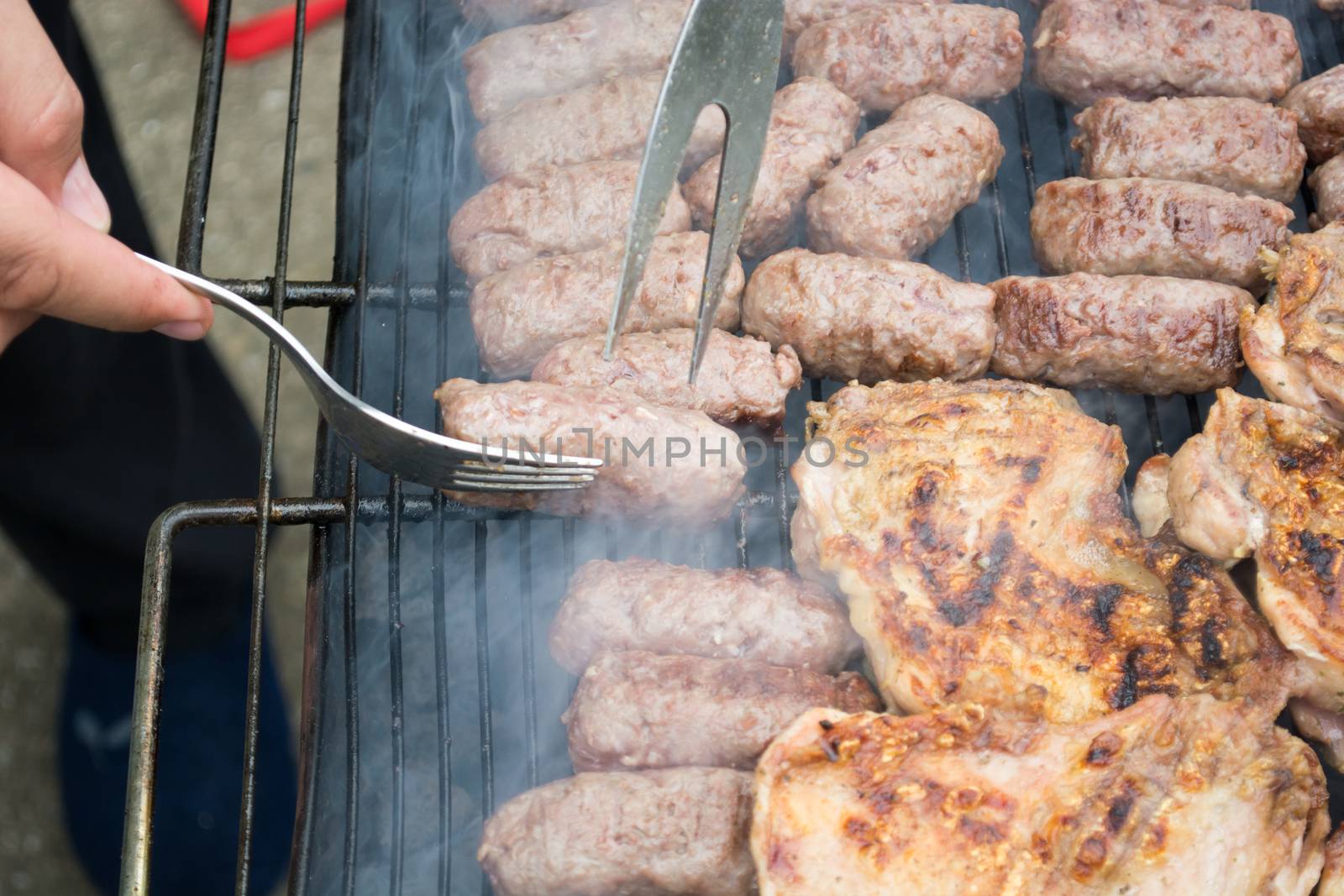 Grilling cevapi and pork chops. Hand visible in the shot