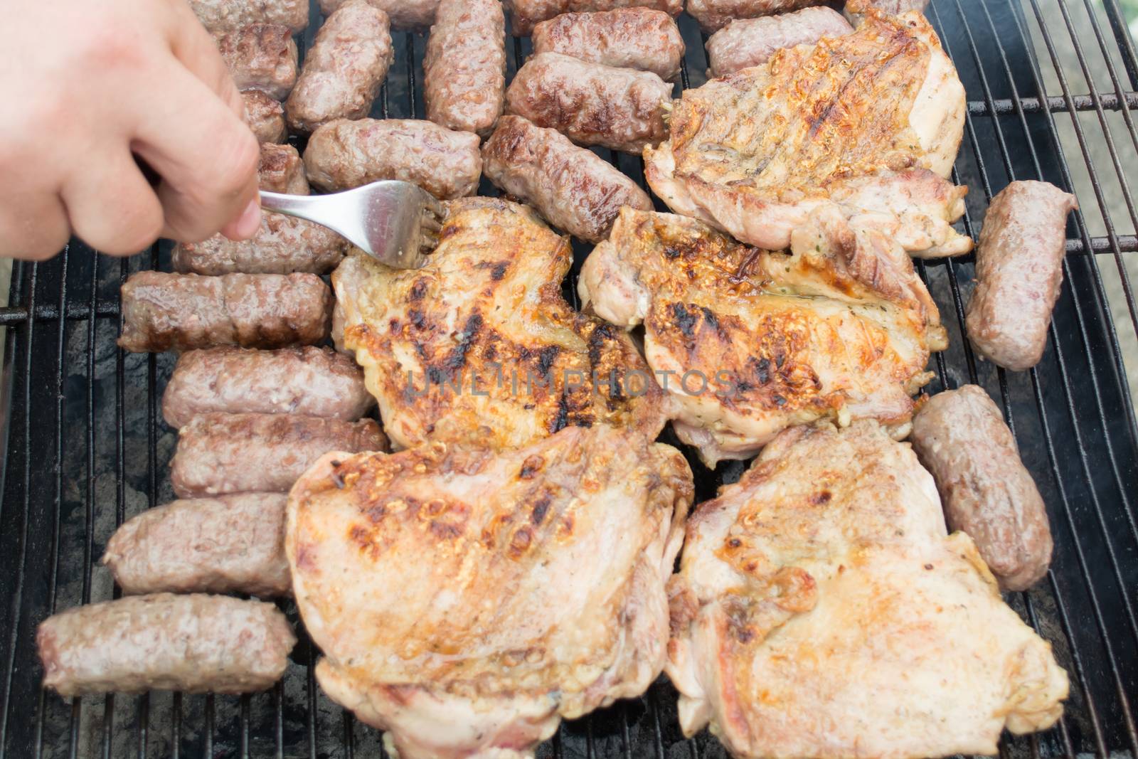 Grilling cevapi and pork chops. Hand visible in the shot