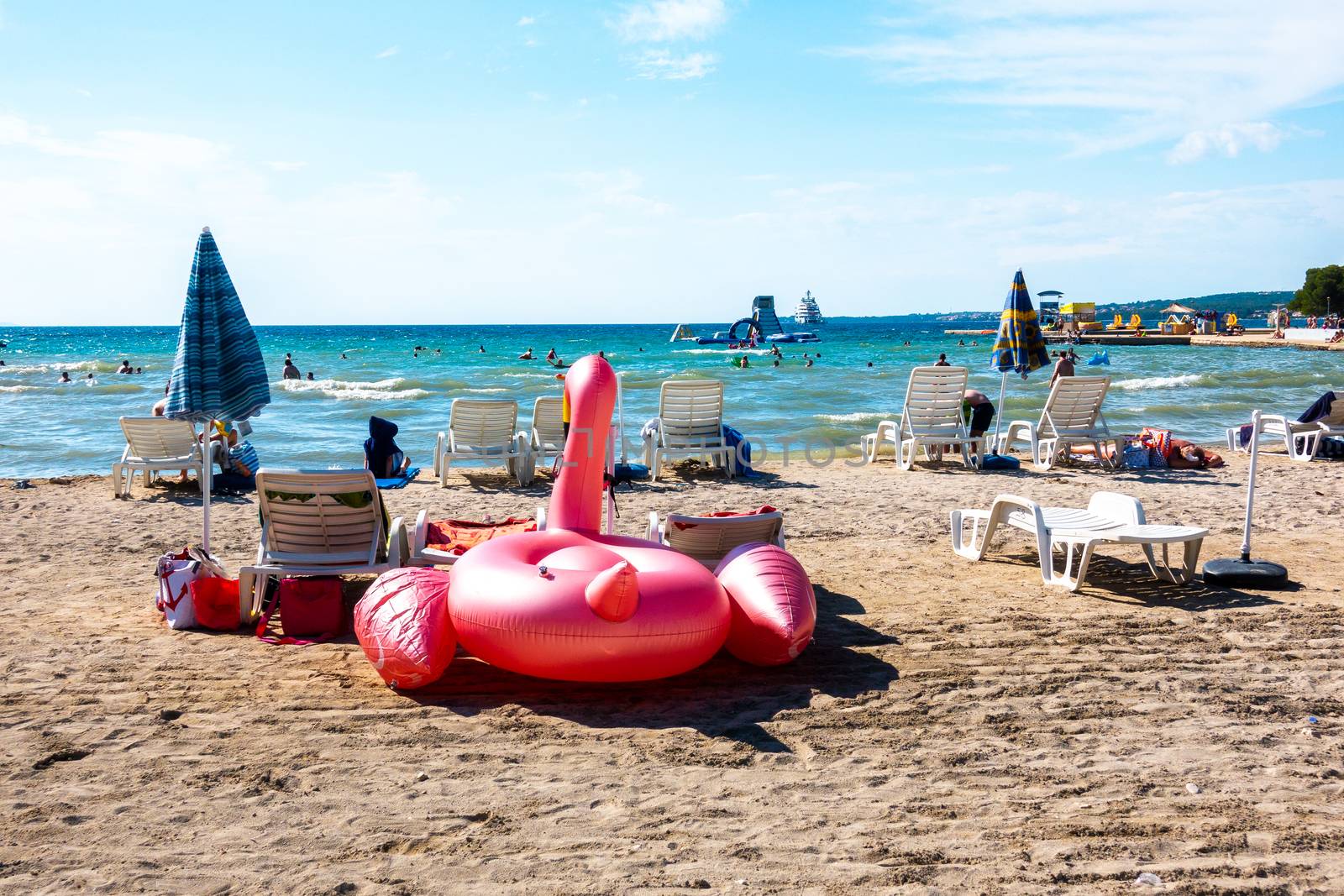 Floatie Flamingo on Luxury sand beach in Borik, Zadar Croatia with sunchairs and people swimming and sunbathing