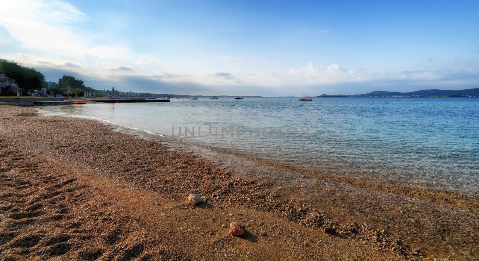 Beach in Turanj, small village in Dalmatia, Croatia, island of Pasman in background, sunchairs, parasols, umbrellas and beach requisites