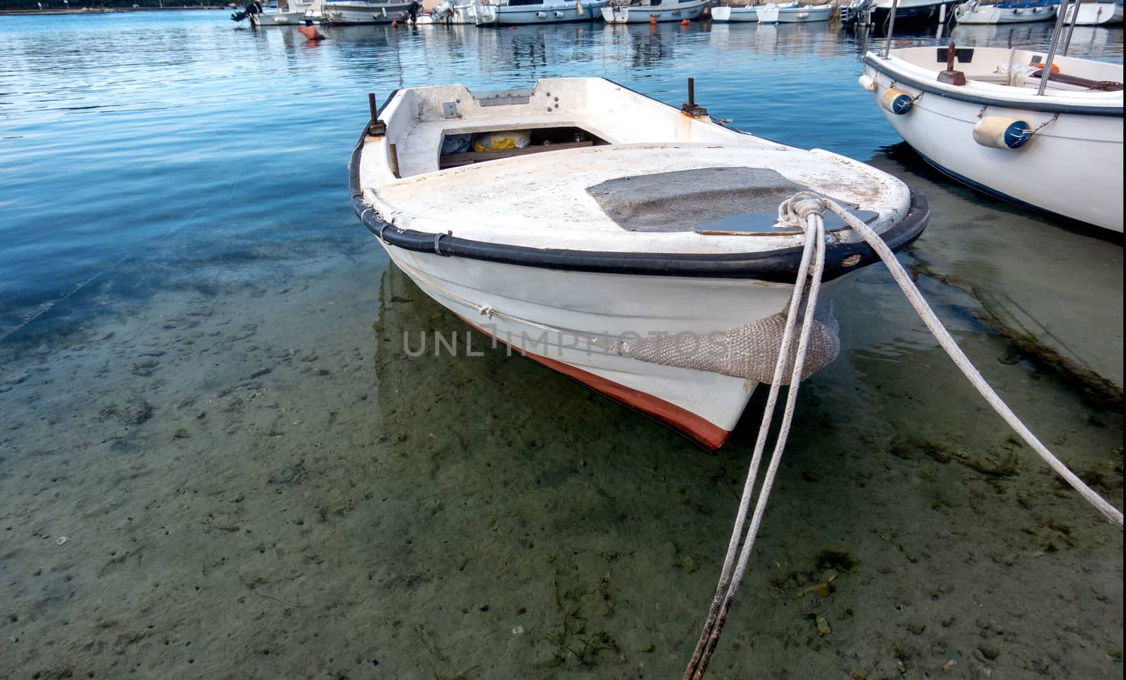 Small traditional wooden fishing boat in harbor, moored to the pier, sky reflecting in water, small water vessel