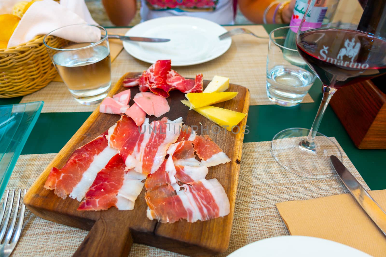 Italian style cold meat plate with cheese on wooden board with pancetta, Prosciutto, cheese and mortadella with glass of red wine, plate and cutlery