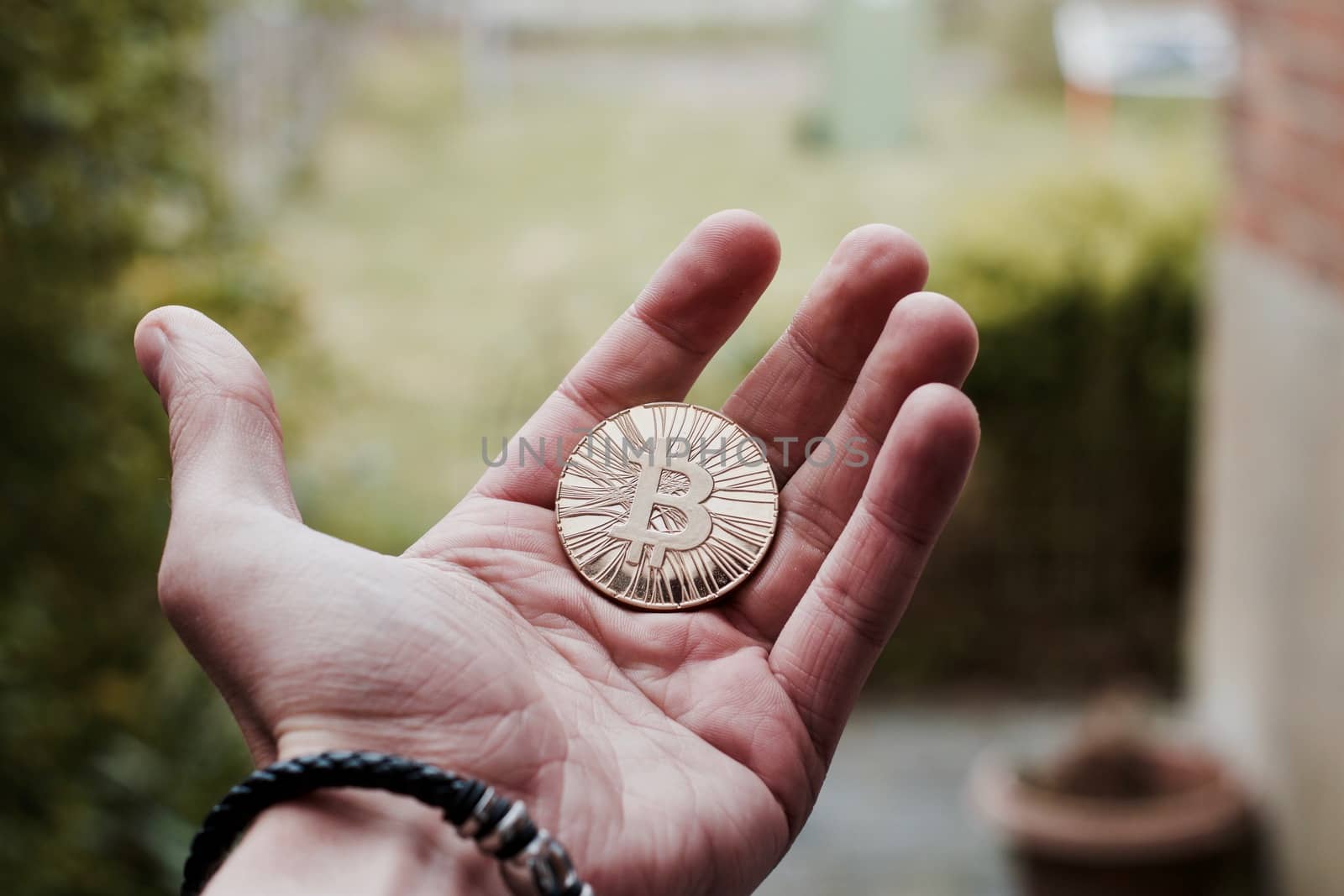 Digital currency physical gold bitcoin coin on man hand with bracelet.