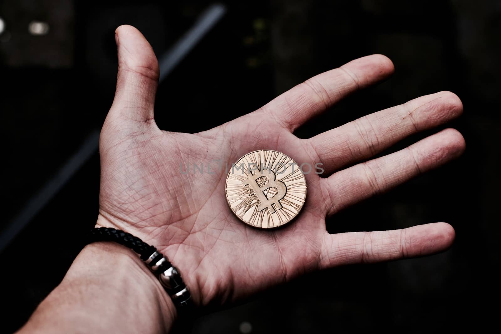 Digital currency physical gold bitcoin coin in man hand with black bracelet.