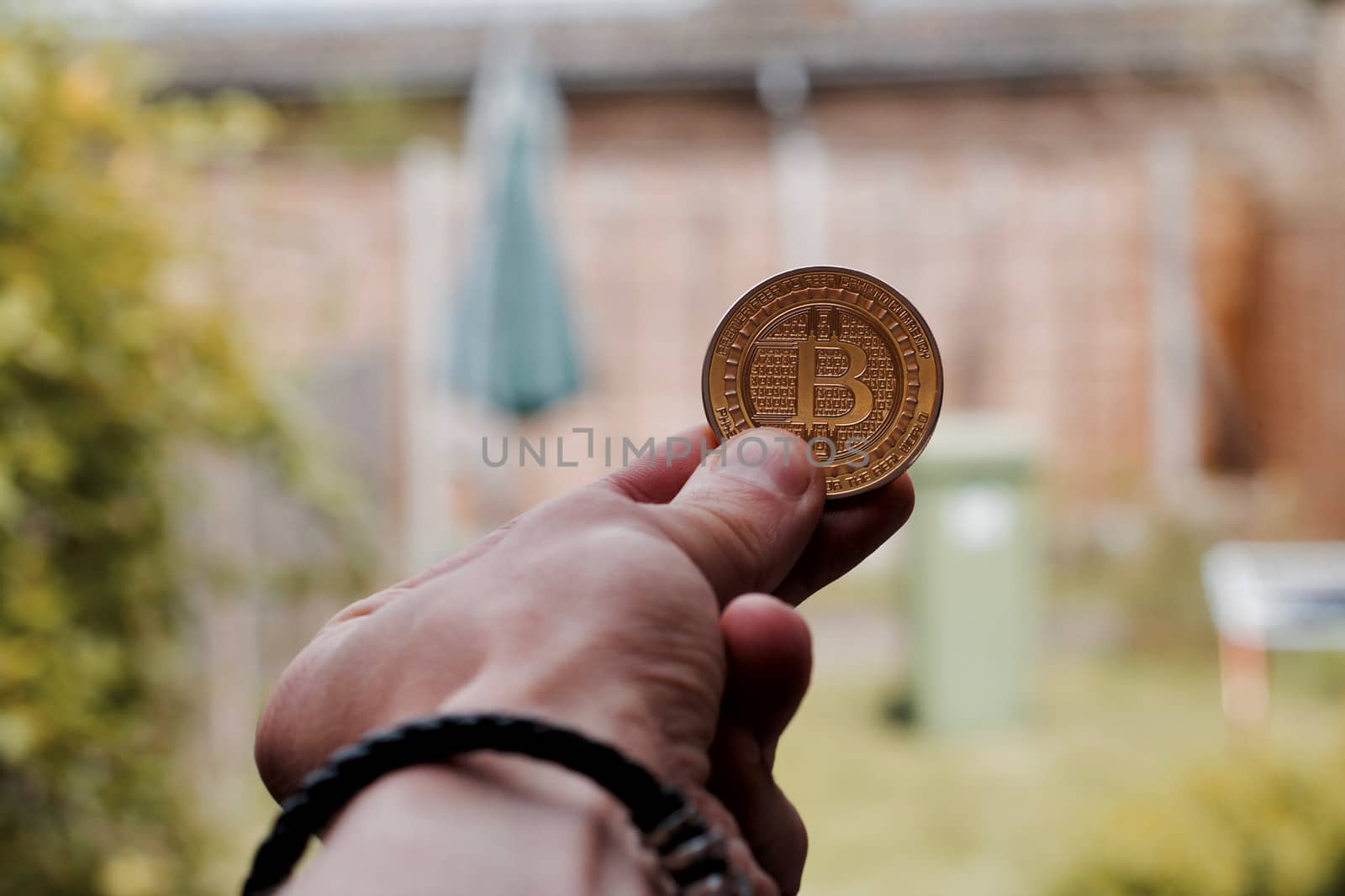 Digital currency physical gold bitcoin coin in man hand with black bracelet.