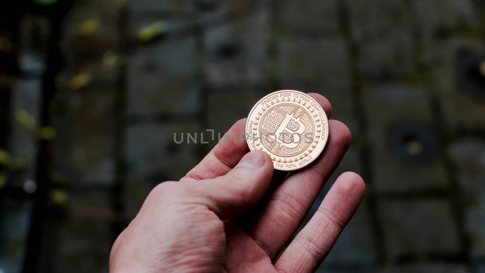 Digital currency physical gold bitcoin coin in man hand with black bracelet.