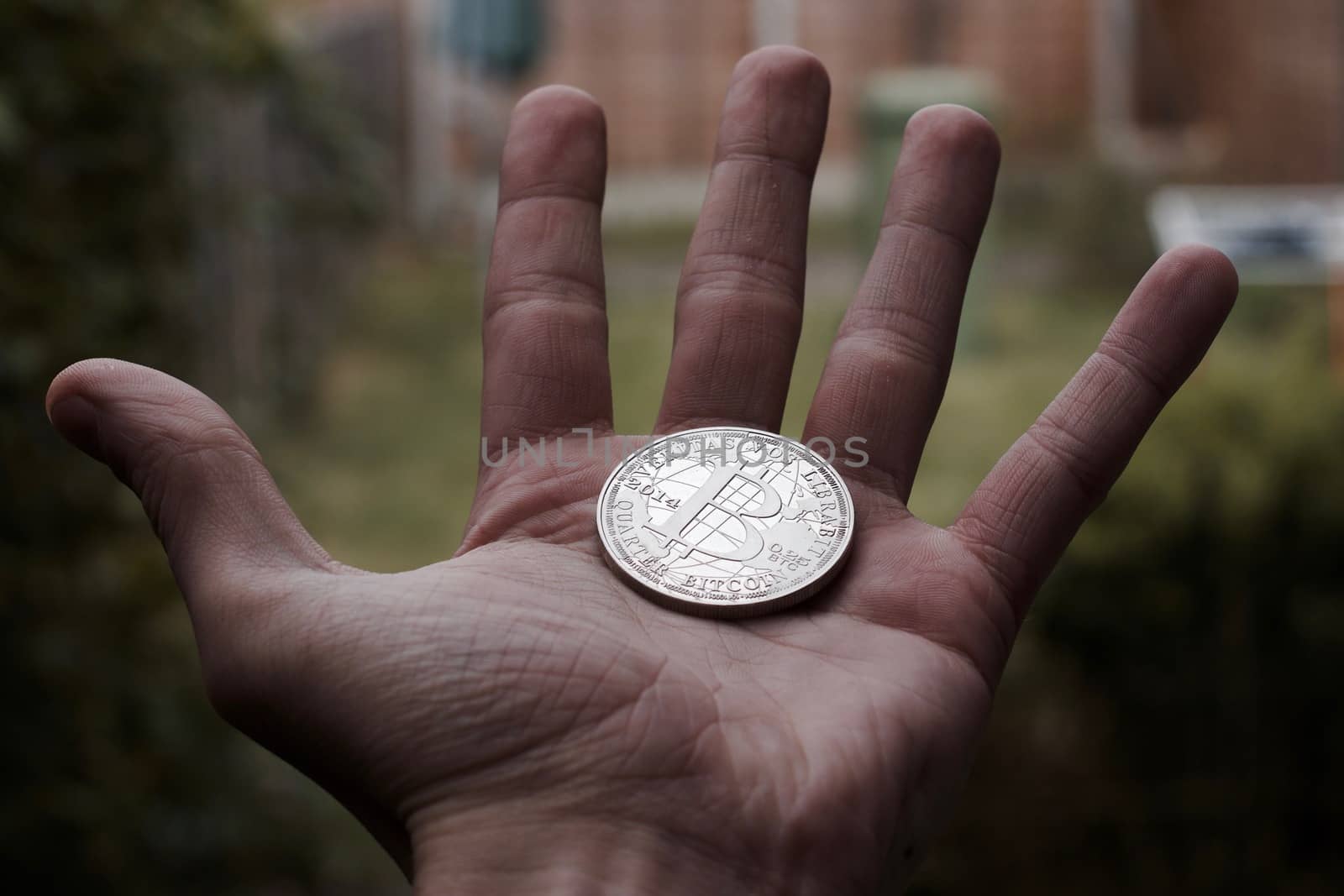 Cryptocurrency physical silver bitcoin coin on man hand outdoor.