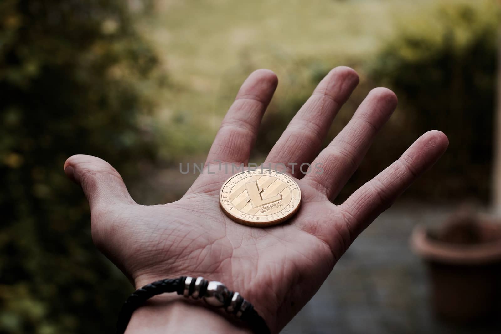 Digital currency physical gold litecoin coin on man hand with black bracelet.
