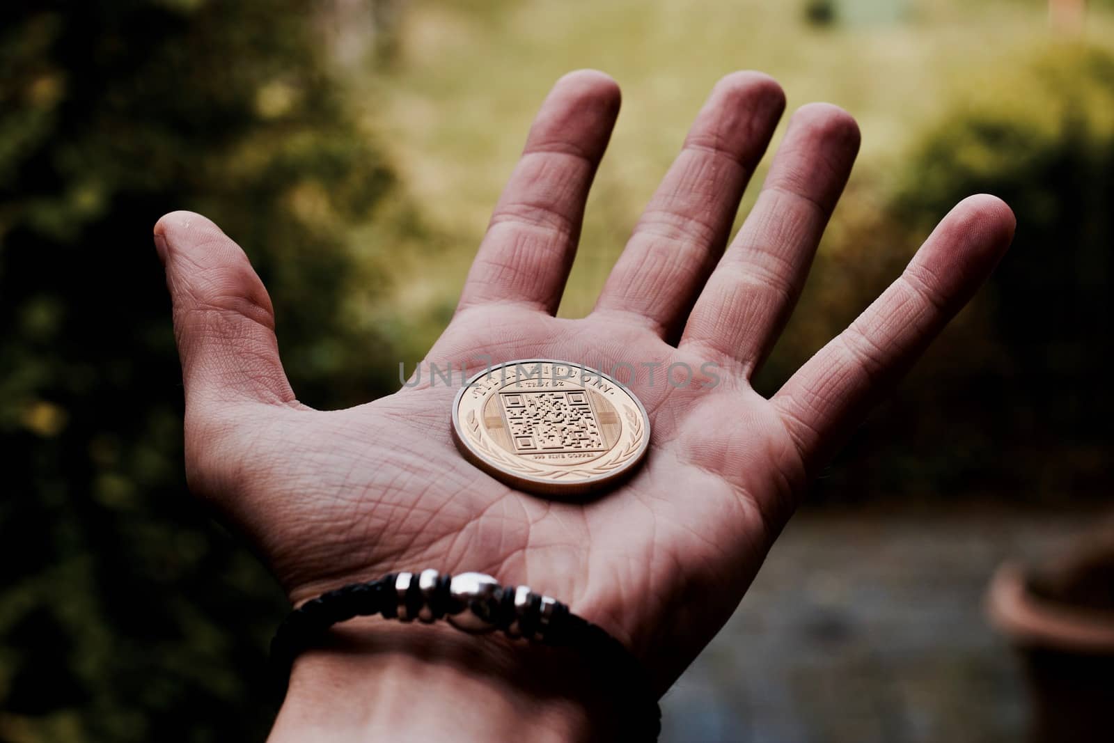 Digital currency physical gold bitcoin coin in man hand with black bracelet.