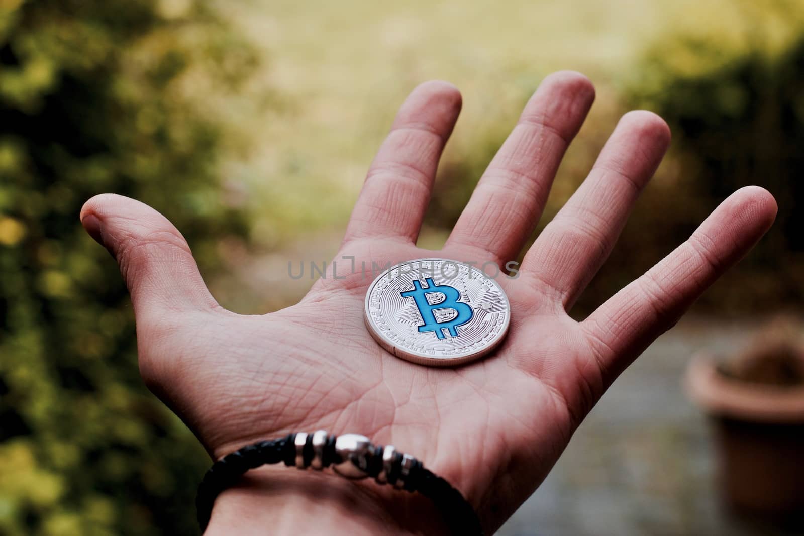 Cryptocurrency physical silver bitcoin coin on man hand with black bracelet outdoor.