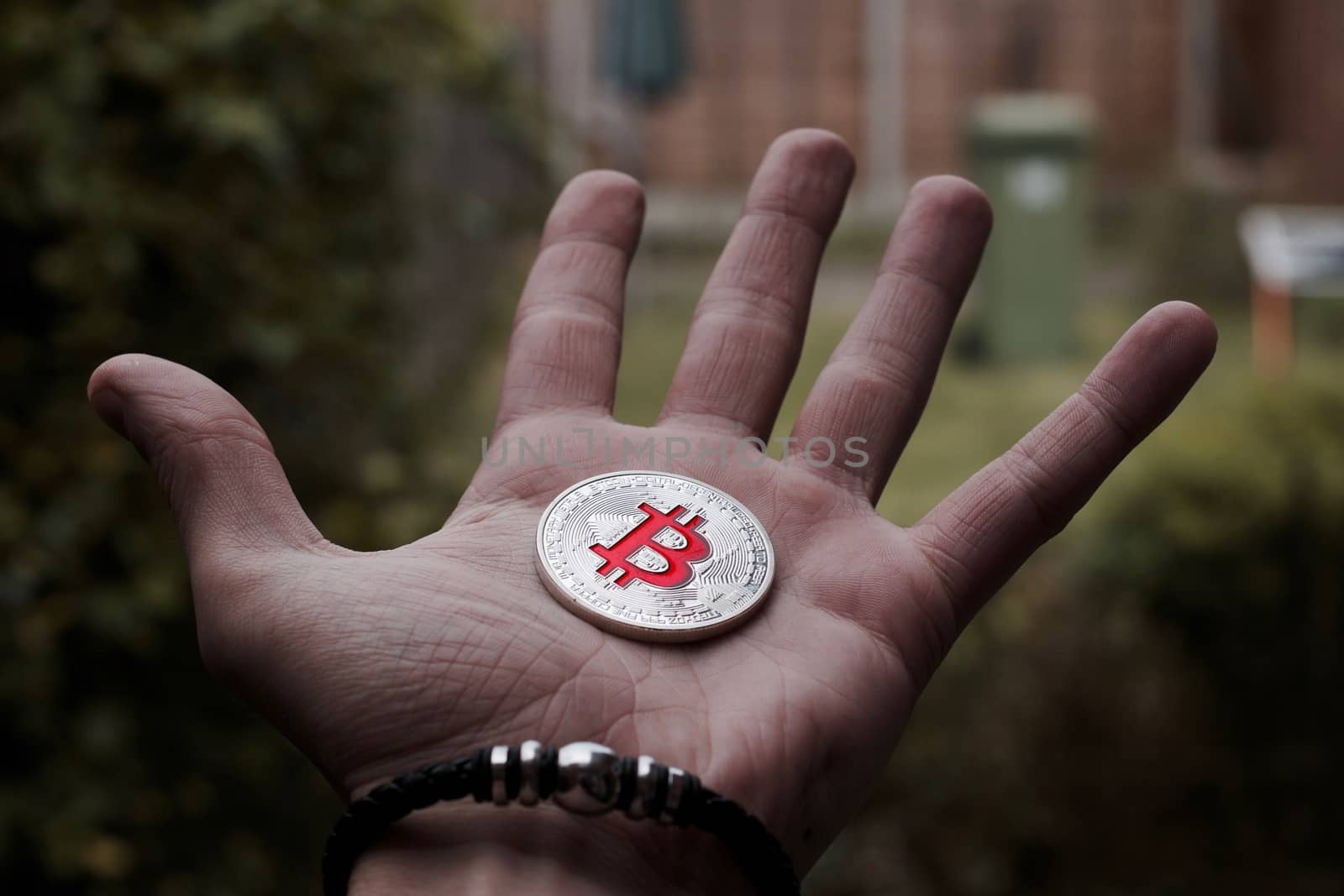Cryptocurrency physical silver bitcoin coin on man hand with black bracelet outdoor.