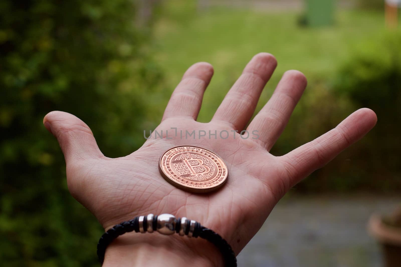 Digital currency physical brass bitcoin coin in man hand with black bracelet.
