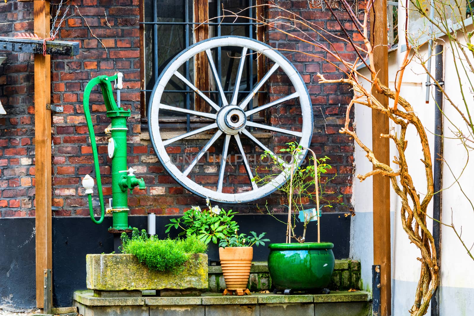 Wooden wagon wheel, water pump on a house wall.           by JFsPic