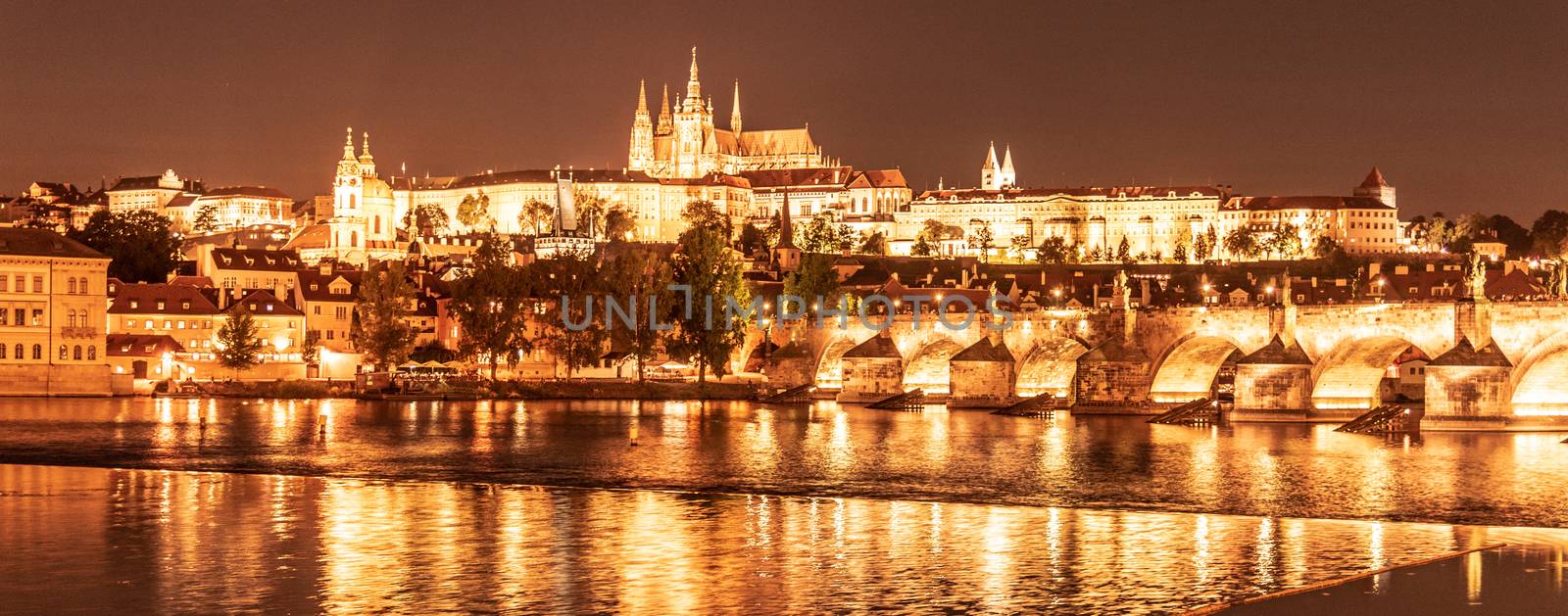 Golden Prague by night. Prague Castle and Charles Bridge reflected in Vltava River. View from Smetana Embankment. Praha, Czech Republic by pyty