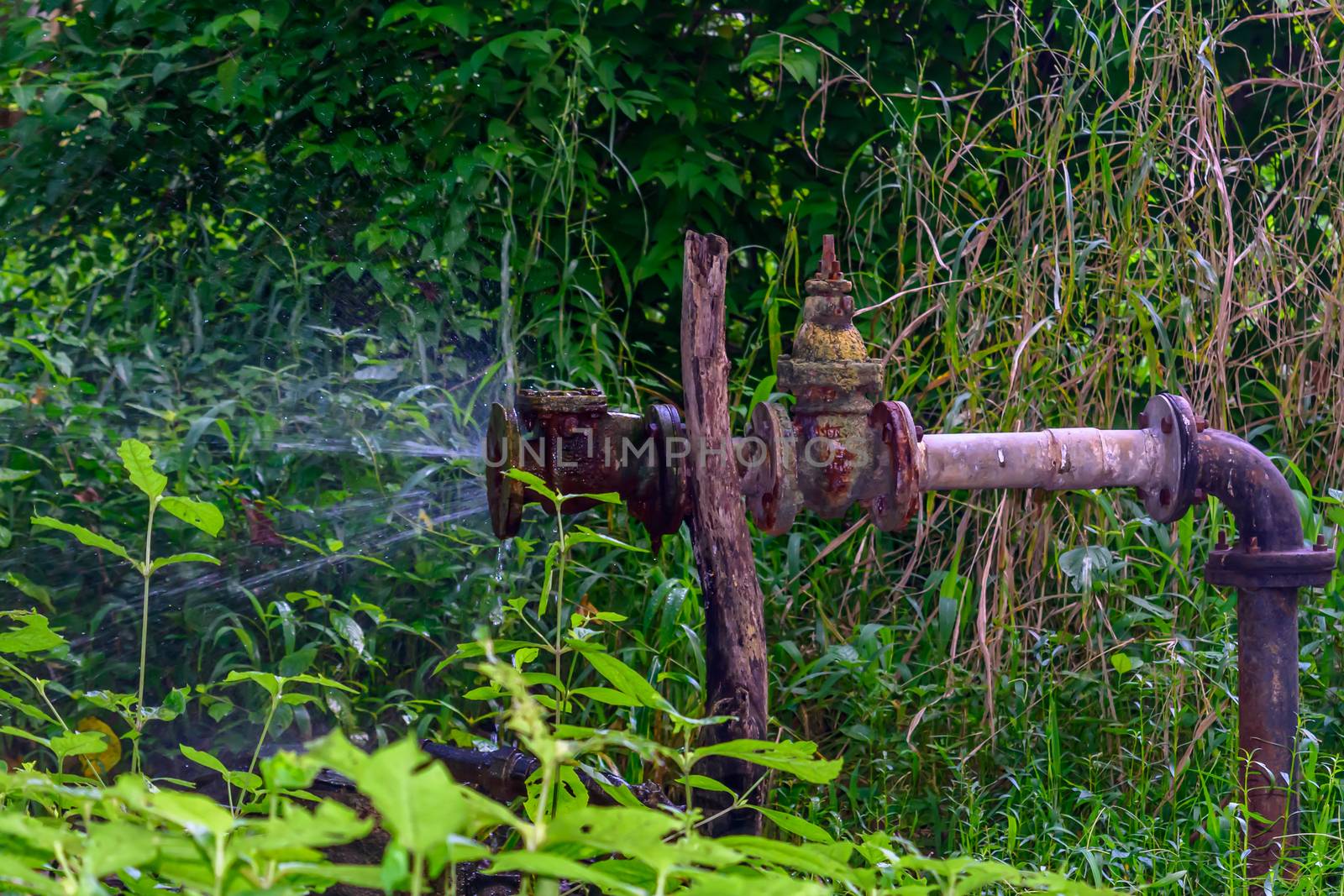 Old iron Metallic water pipe leaking. Rusty burst pipe spraying water.