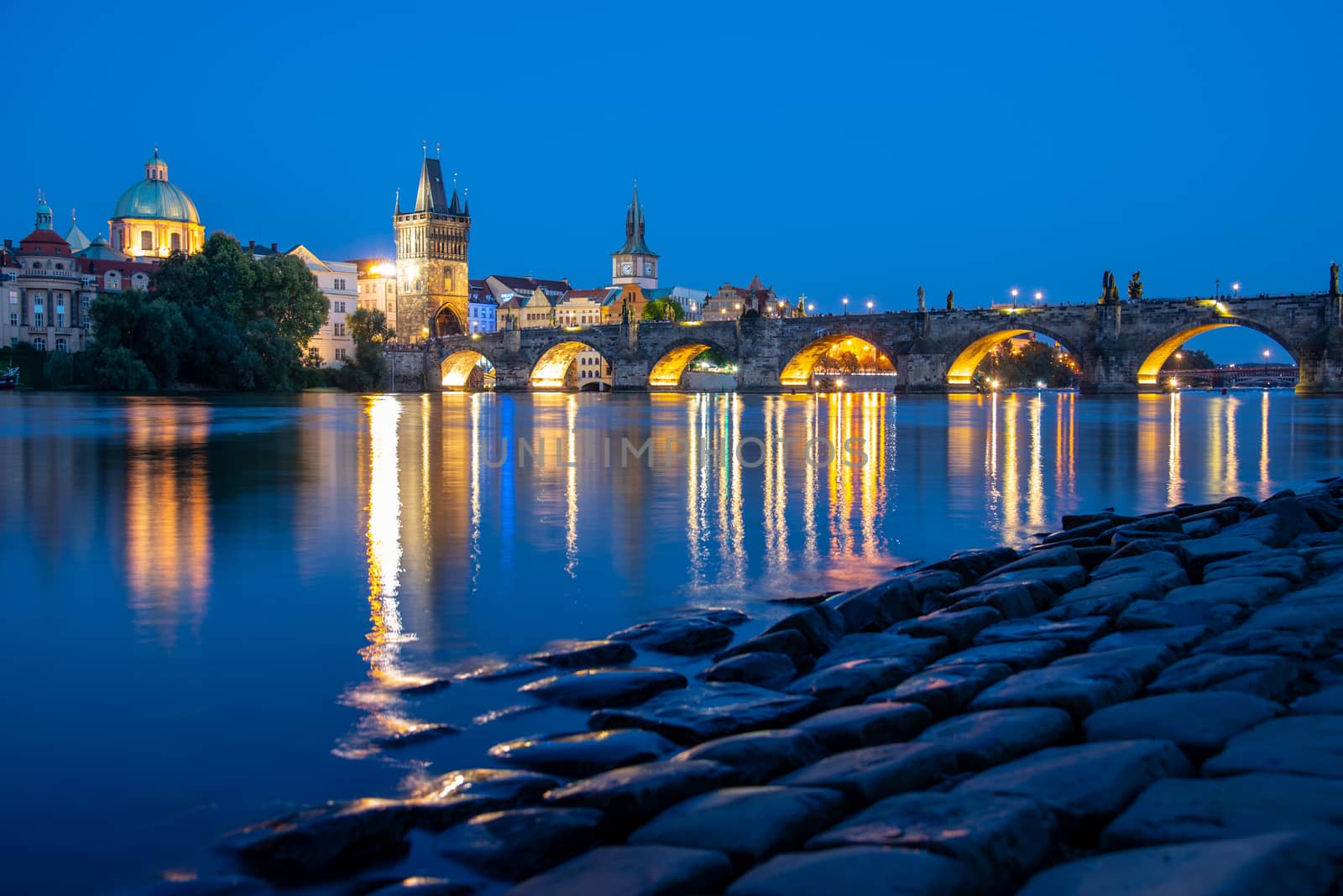 Illuminated Charles Bridge reflected in Vltava River. Evening in Prague, Czech Republic.