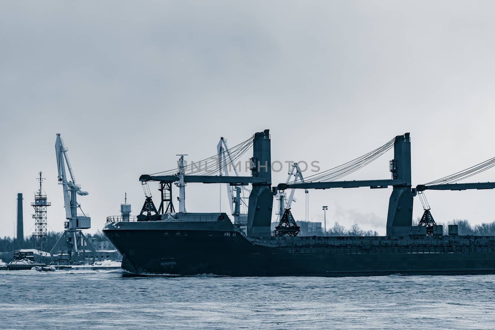 Blue bulk carrier sailing to the sea in cold winter. Monochrome
