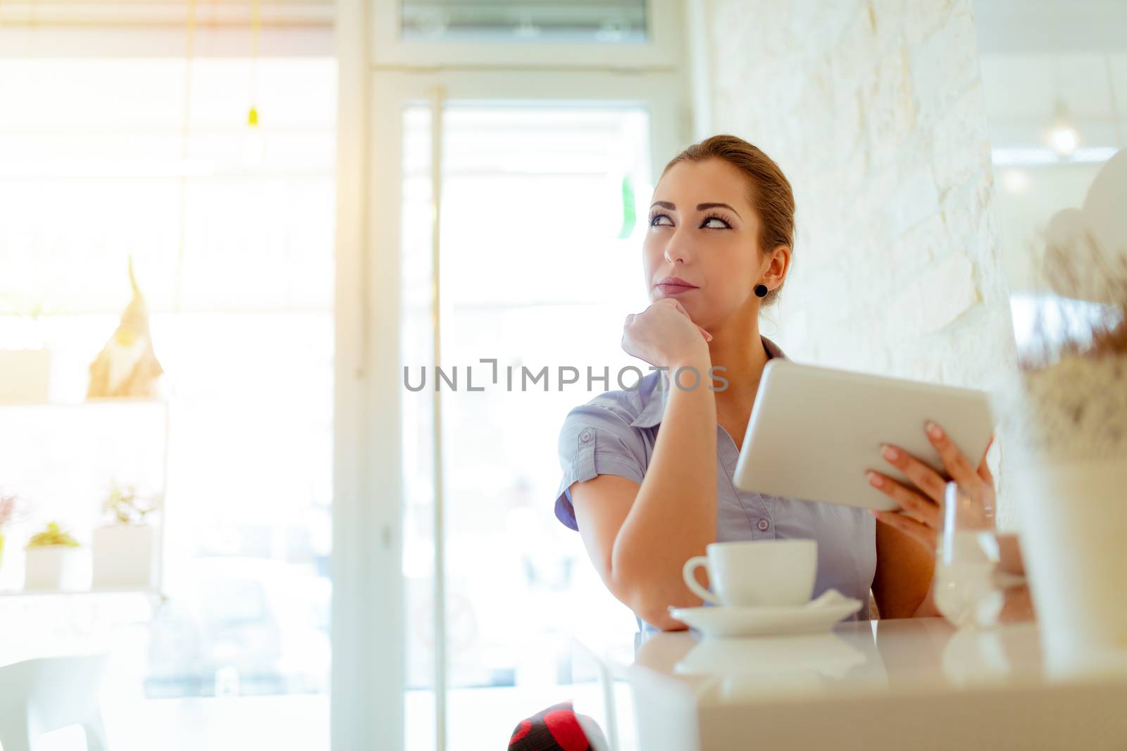 Young pensive businesswoman on a break in a cafe. She is using digital tablet and drink coffee. 