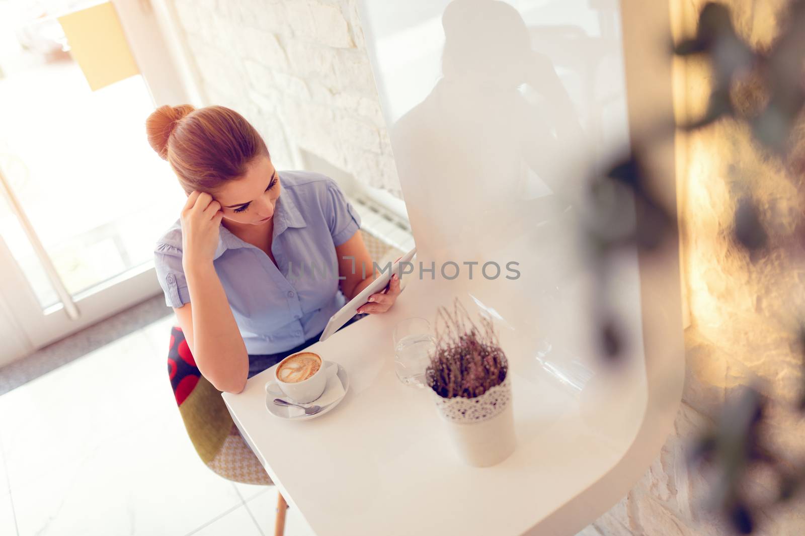 Young smiling businesswoman on a break in a cafe. She is using digital tablet and drink coffee. 