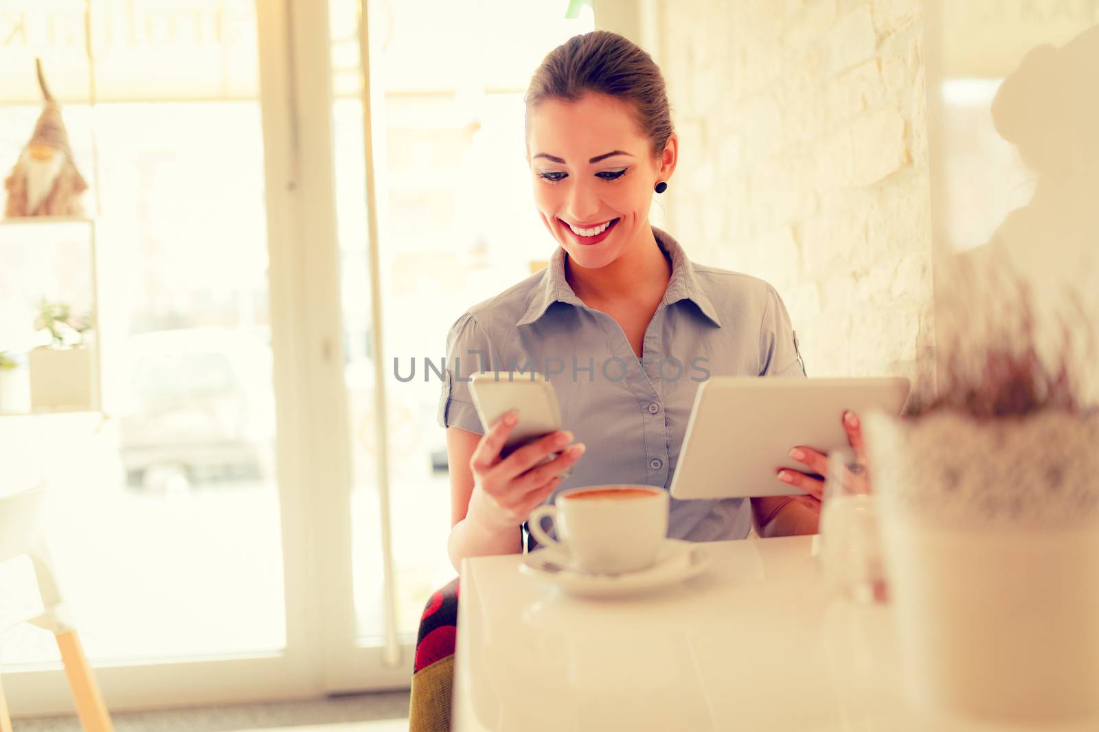 Young smiling businesswoman on a break in a cafe. She is using digital tablet and drink coffee. 