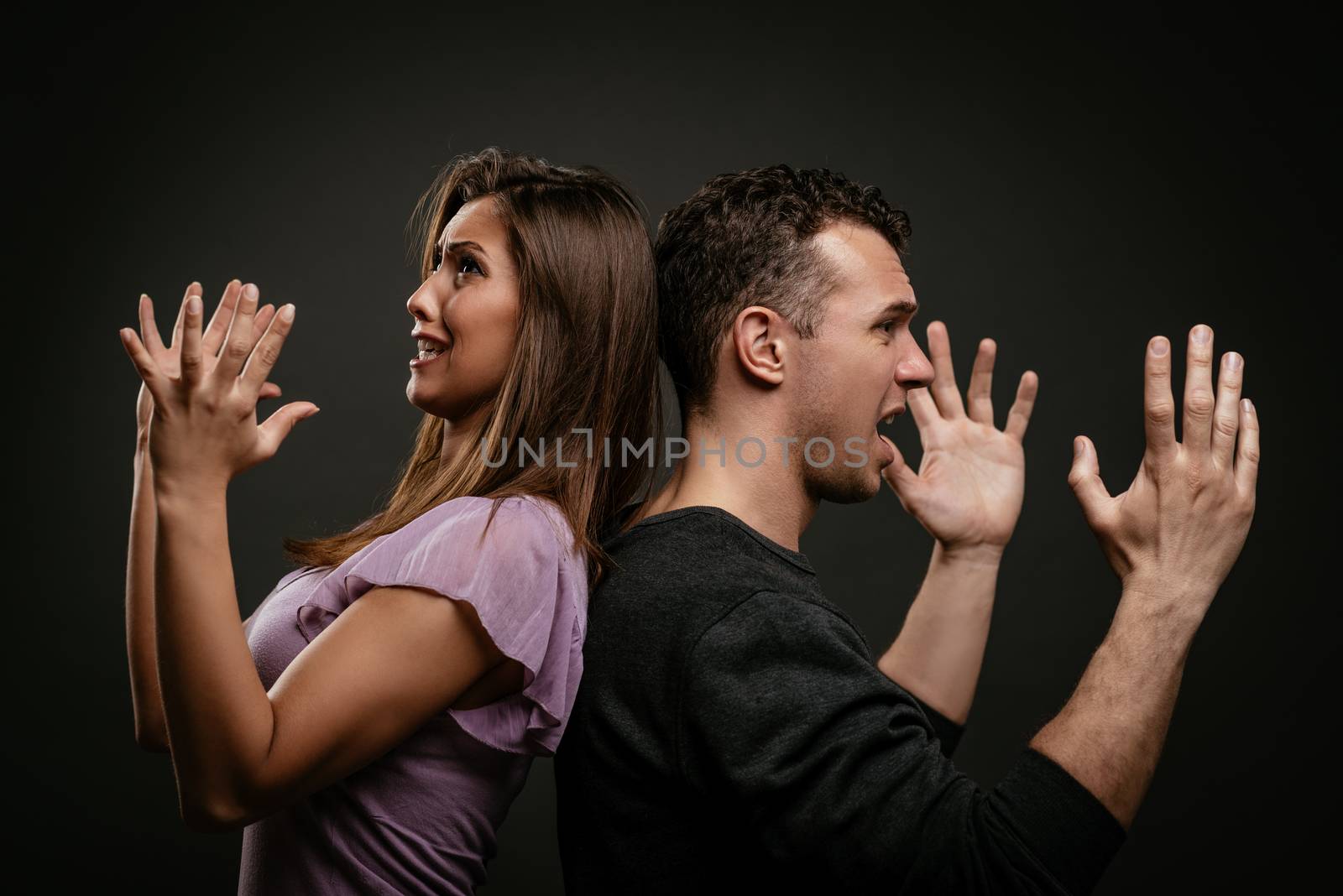 Angry young couple standing back to back and shouting.
