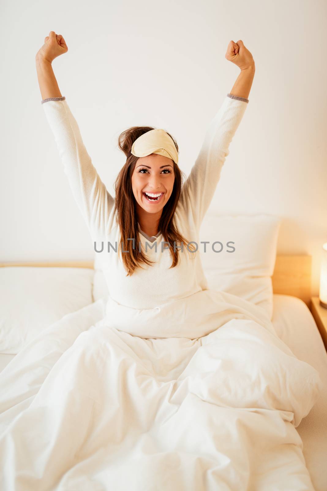Young beautiful woman with sleeping mask sitting in the bed in morning and stretching.