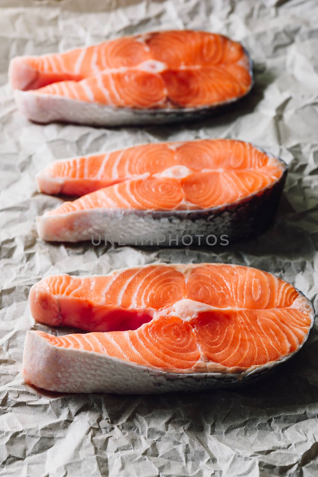 Three Raw Salmon Steaks on Parchment Paper. Vertical.
