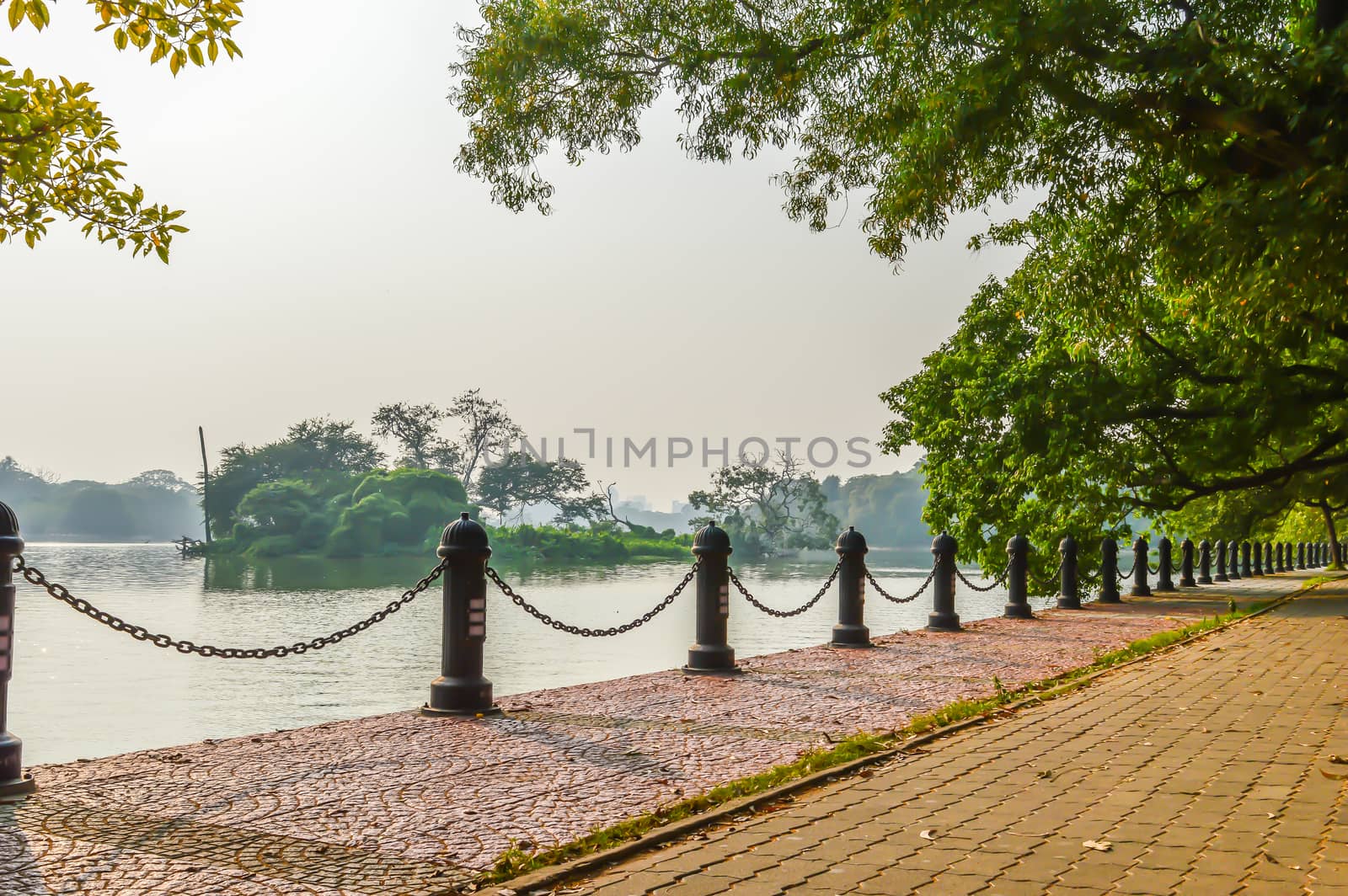 Beautiful green park & blue clear sky landscape. A line of fence and red brick path on a summer's day. The Subject of the image is adventure, inspiration, exciting, hopeful, bright, sensational, tranquil, calm, stormy, stunning. This photography is taken in as landscape style. This photograph may be used as a background, wallpaper, screen saver.