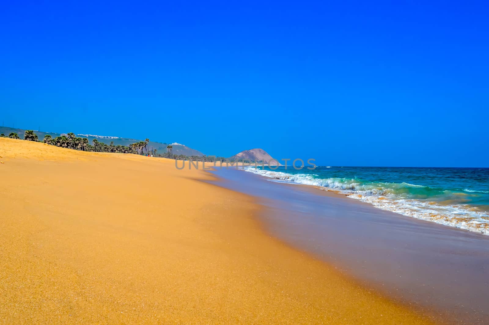 Wild Empty Tropical beach, vibrant yellow sand, bright blue sky, crystal clear waters with water crashing on the shore at daytime on a sunny day by sudiptabhowmick