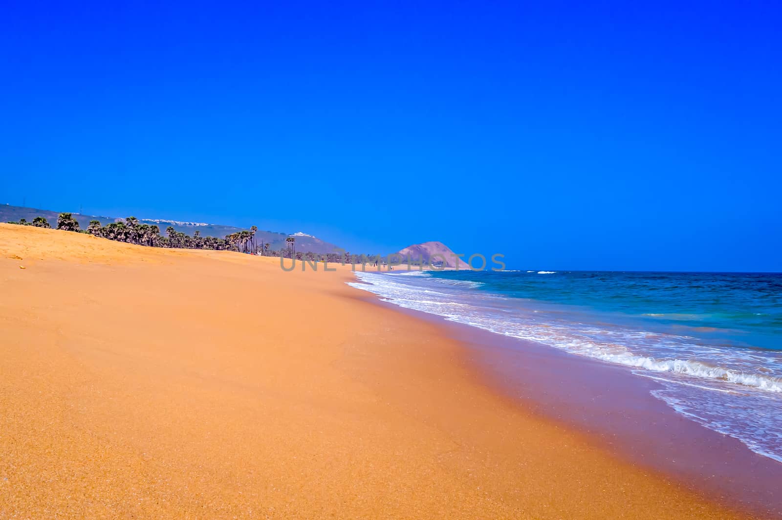 Wild Empty Tropical beach, vibrant yellow sand, bright blue sky, crystal clear waters with water crashing on the shore at daytime on a sunny day in in as landscape style may be used as a background, wallpaper, screen saver Travel vacation concept. The image is exciting, bright, sensational, tranquil, calm, stunning