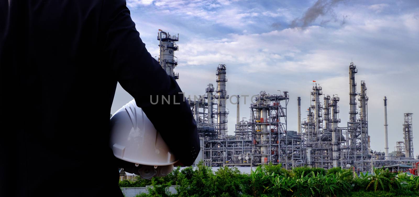 The engineer is holding a safety helmet on large industry background. The construction manager on the industry background.