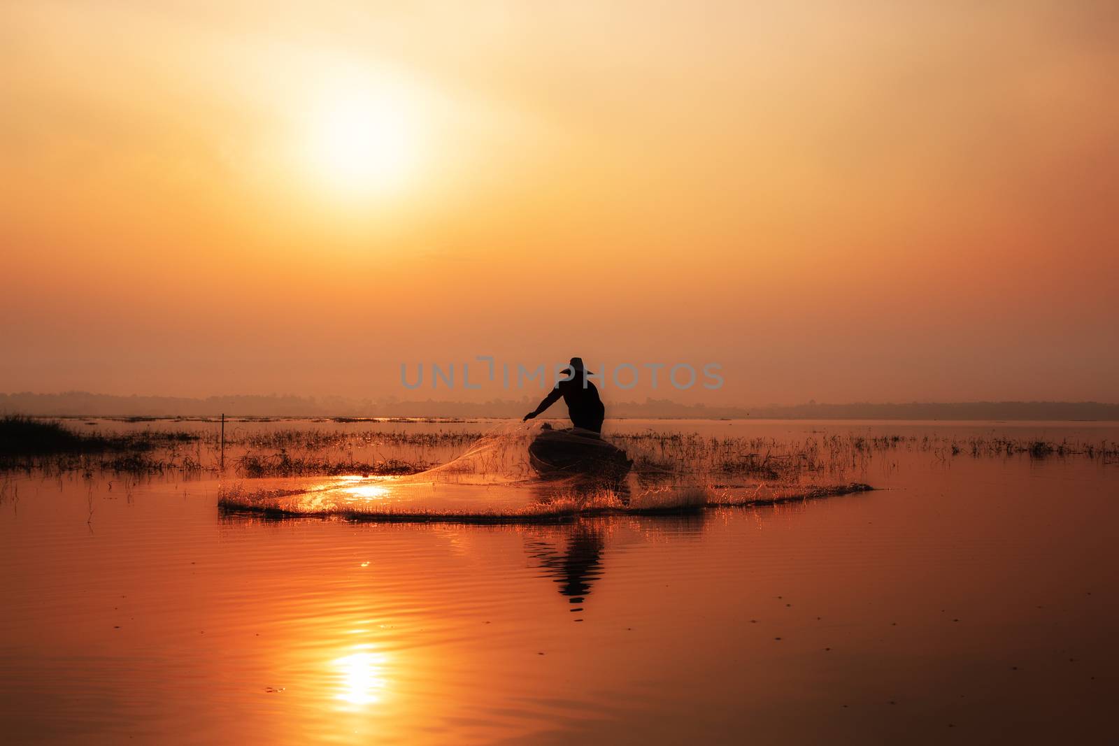 Silhouette of fishermen casting for catching the fish on the wooden boat at the lake in the morning. Thailand lifestyle.