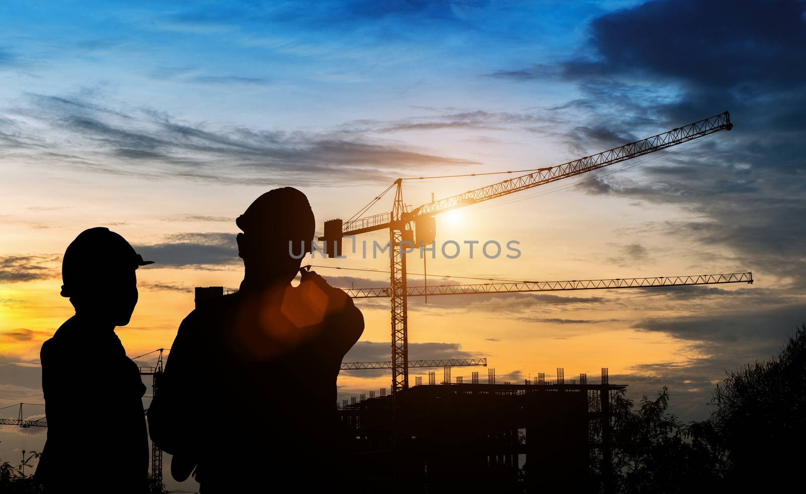 Silhouette engineers are standing survey work on construction over blurred Worker in  construction site and sunset.