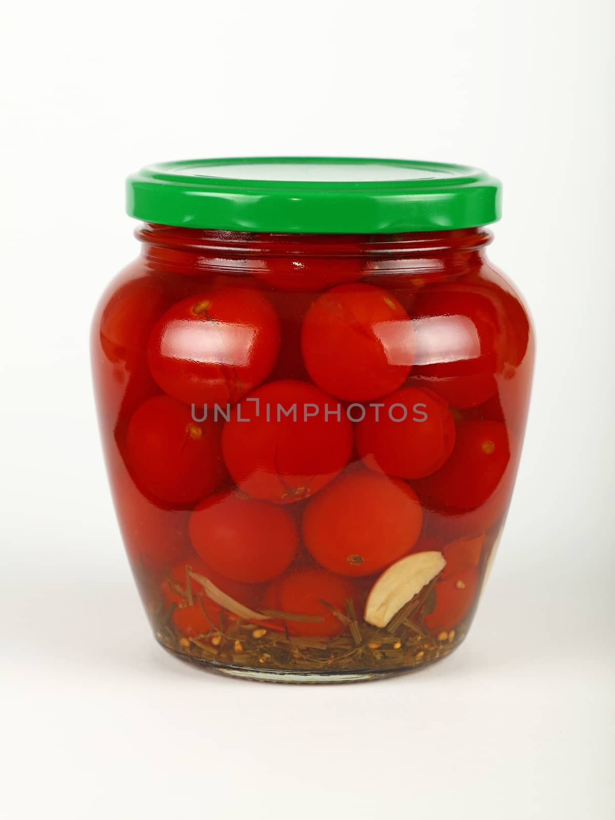 Close up of one glass jar of pickled small red cherry tomatoes with green lid over white background, low angle side view