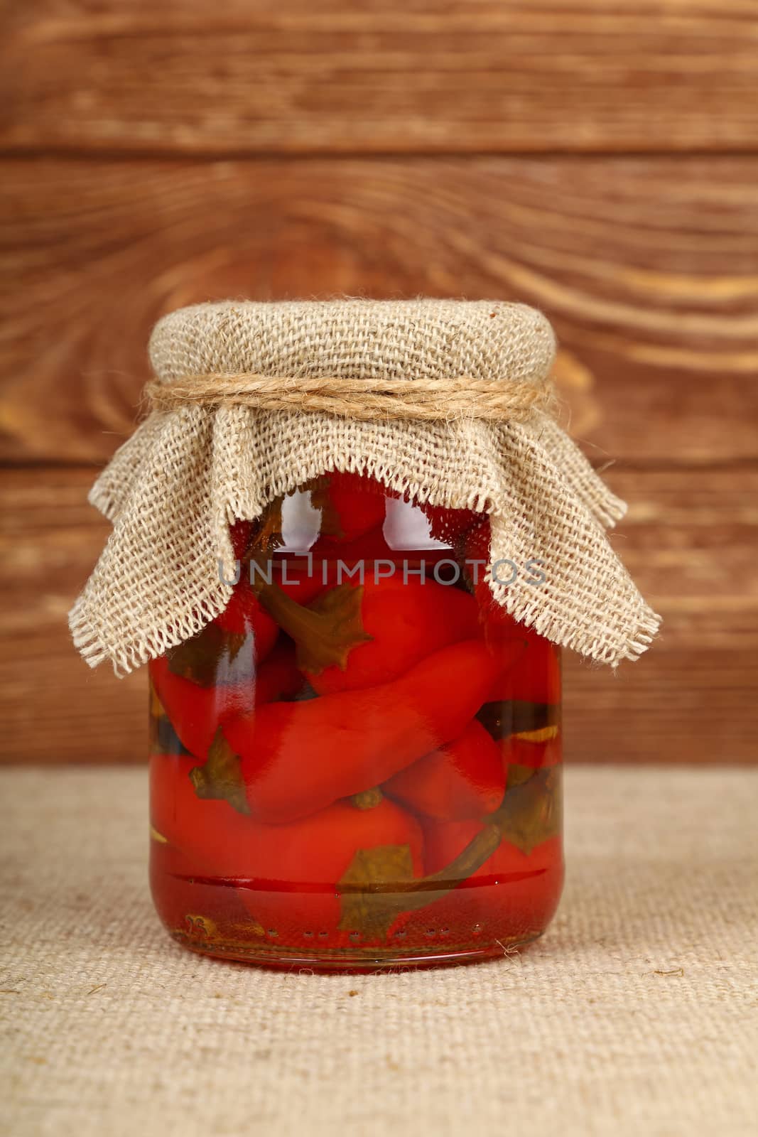 Jar of pickled red hot chili peppers on table by BreakingTheWalls