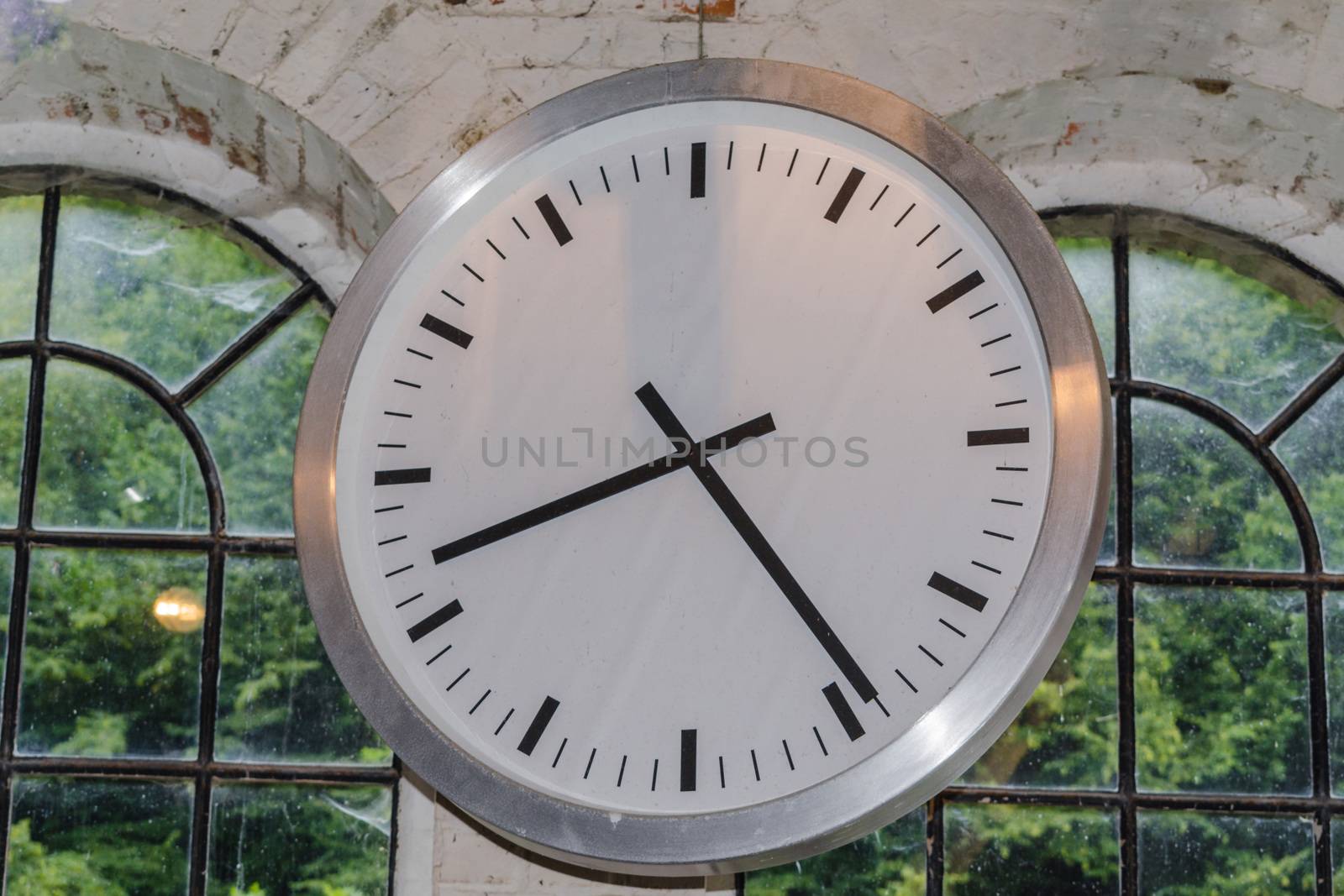 Large clock in front of the window in an industrial factory on a brick wall.