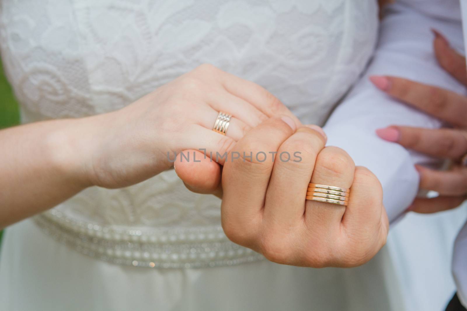 Couple holding hands with rings against white wedding dress