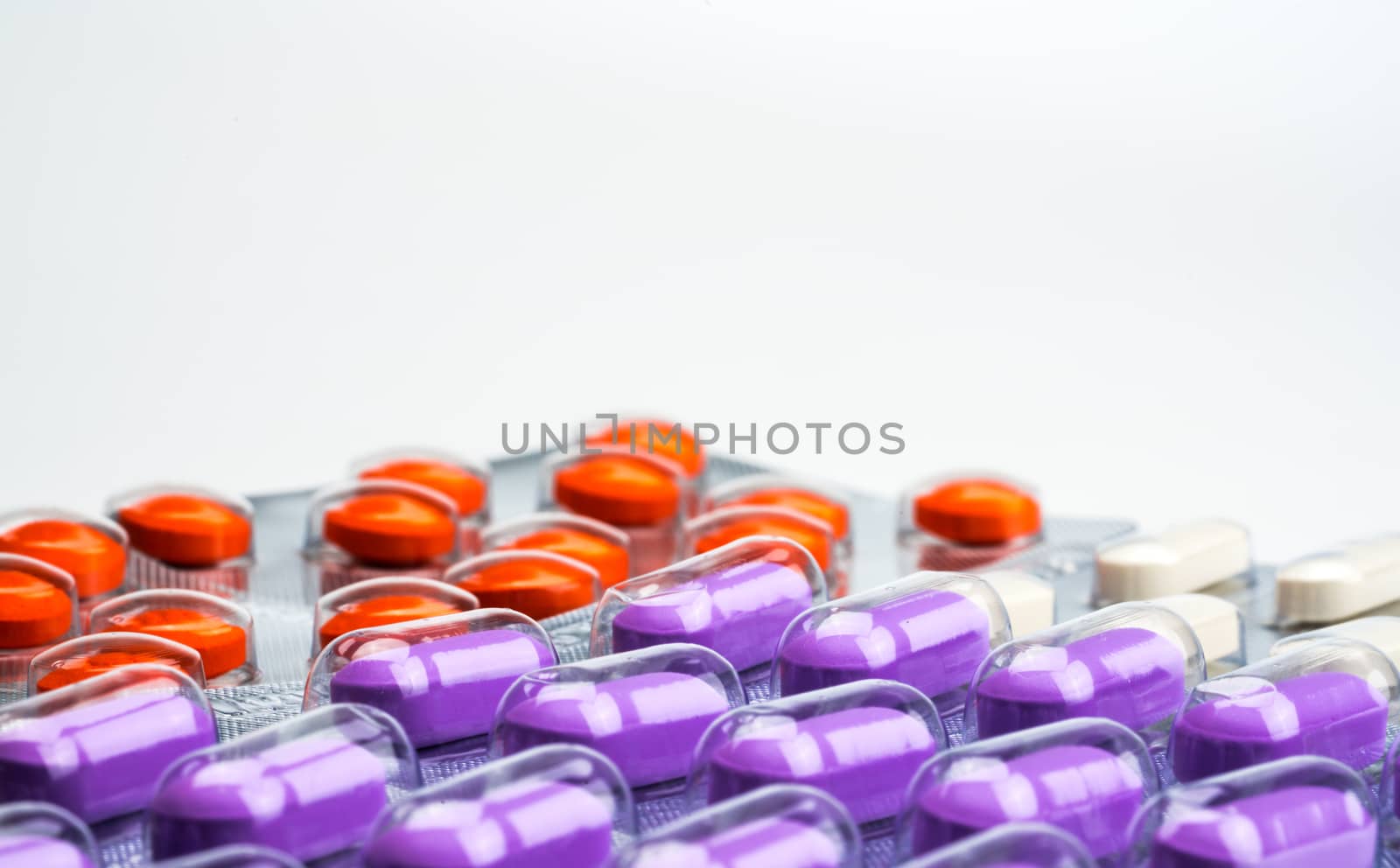 Macro shot detail of orange, purple and white tablets pills in blister pack on white background. Colorful medicine for relieve pain. NSAIDs drug for anti-inflammation can cause gastric ulcer. Pharmaceutical packaging industry. Pharmacy background. Global healthcare concept.