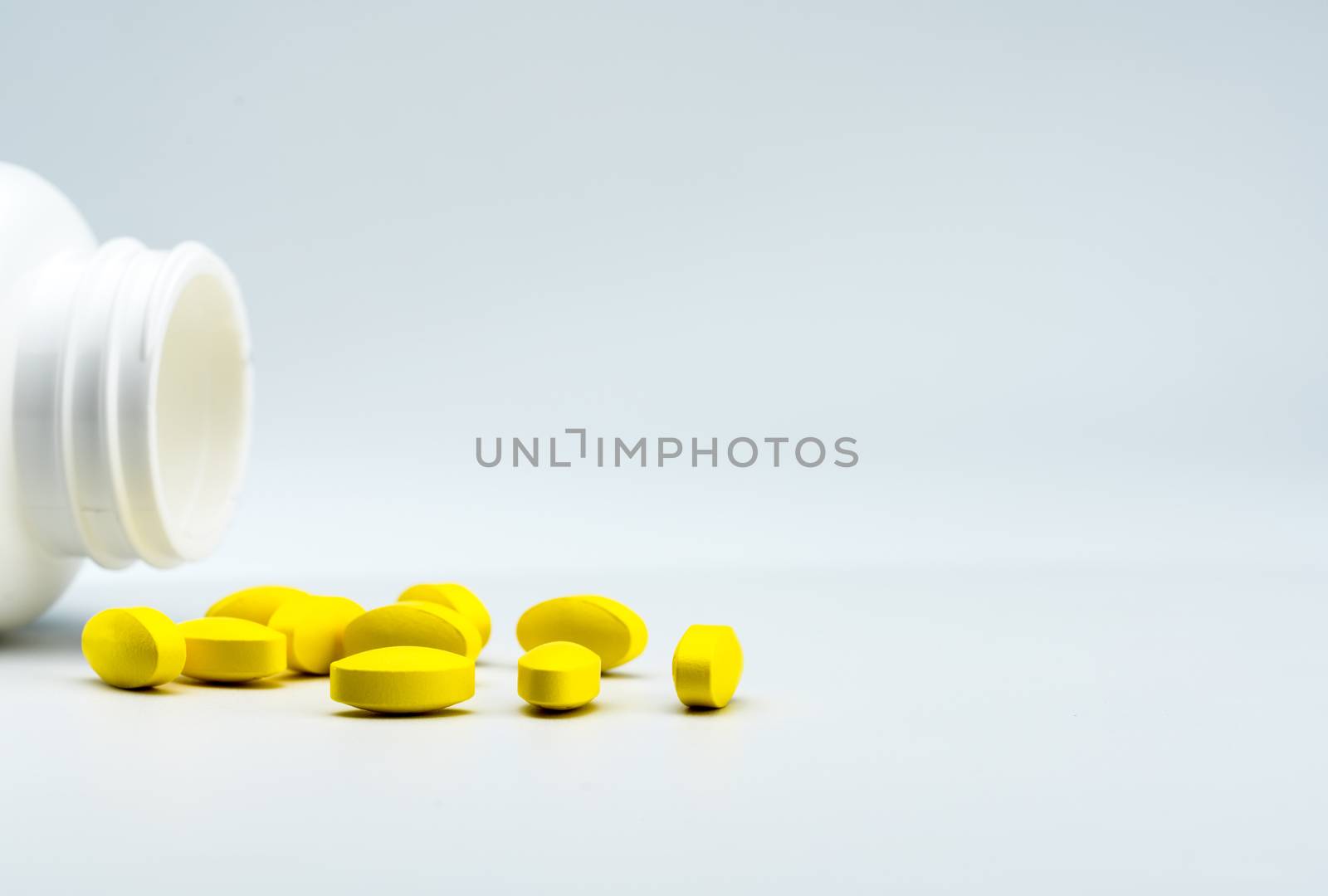 Yellow oval tablet pills and opened white bottle on white background with beautiful creative pattern and copy space for text. Mild to moderate pain management. Pain killer medicine. Pharmaceutical industry. Pharmacy background. Global healthcare concept. NSAIDs drug.