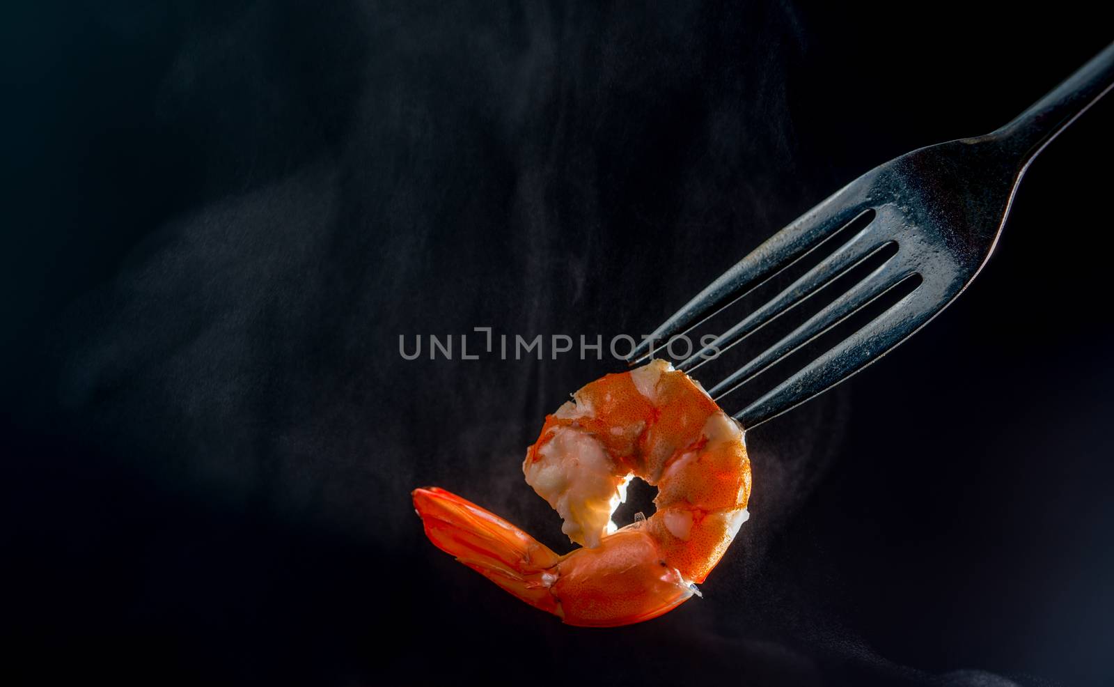 Steamed shrimp on fork isolated on dark background with copy space. Seafood buffet in restaurant concept. Use for seafood buffet promotions advertising