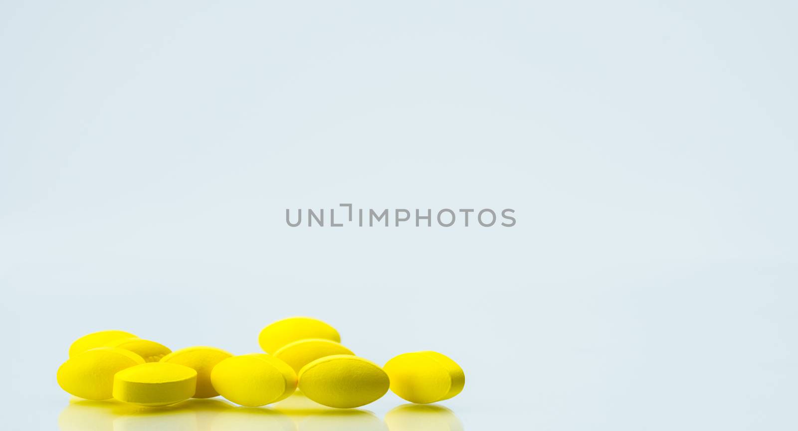 Pile of yellow oval tablet pills on white background with copy space for text. Mild to moderate pain management. Pain killer medicine. NSAIDs drug. Pharmaceutical industry. Pharmacy and pharmacology background. Global healthcare concept. by Fahroni