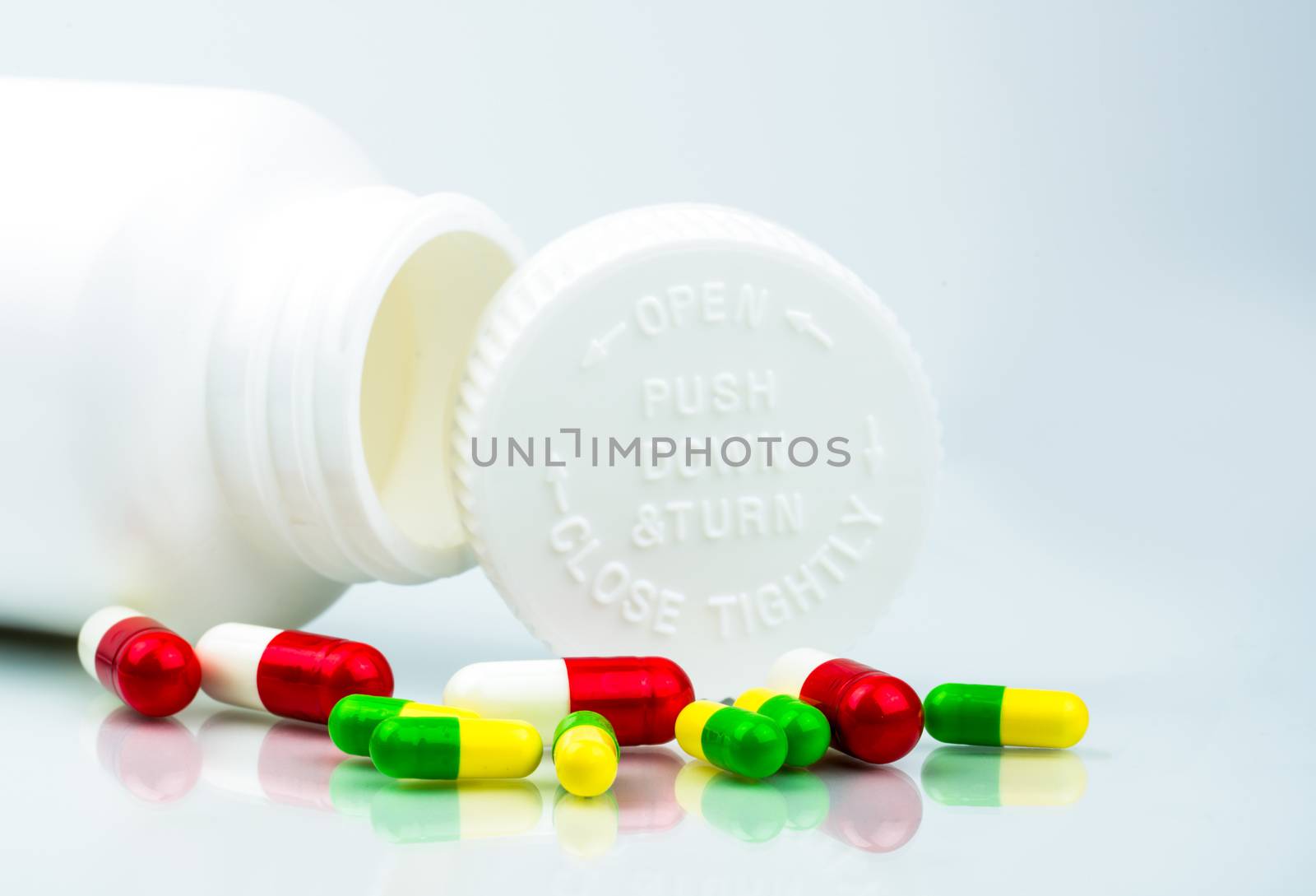 Colorful pills on white background and plastic bottle with blank label and copy space. Childproof packaging. Child resistant pill container. Push down and turn cap. Global healthcare concept. Pharmaceutical packaging industry. Pharmacology and drug interactions concept. Pharmacy background.