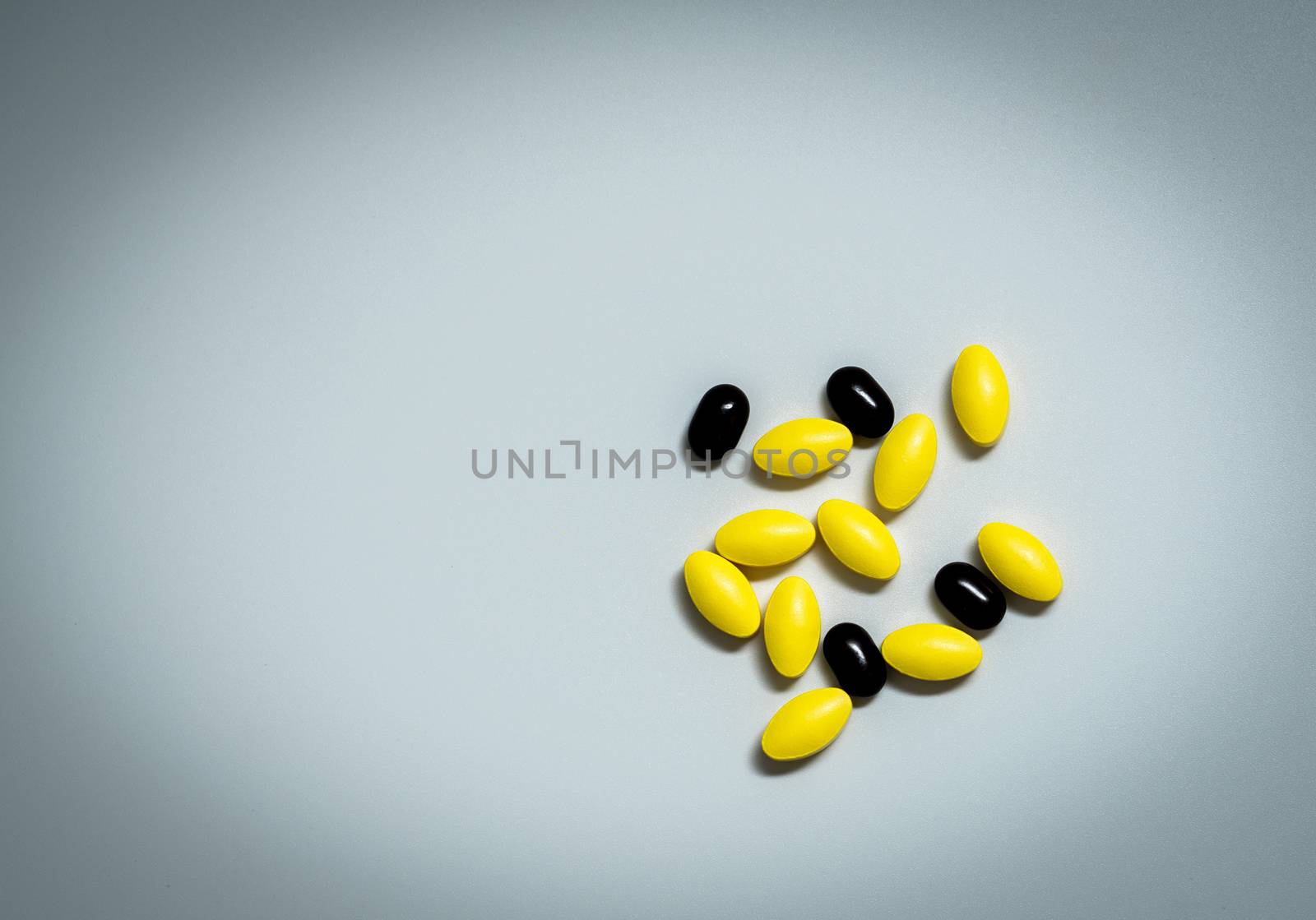 Macro shot of yellow oval tablet pills and black tablets pills on white background with copy space for text. Global healthcare concept. Pharmacology and drug interactions concept. Pharmaceutical industry. Pharmacy background. by Fahroni