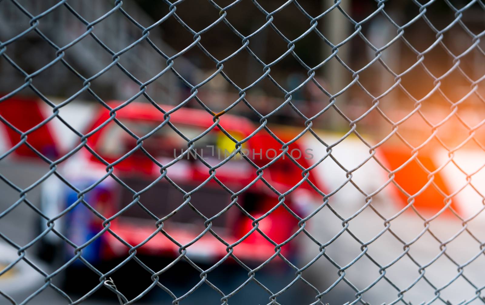 Motorsport car racing on asphalt road. View from the fence mesh netting on blurred car on racetrack background. Super racing car on street circuit. Automotive industry concept.