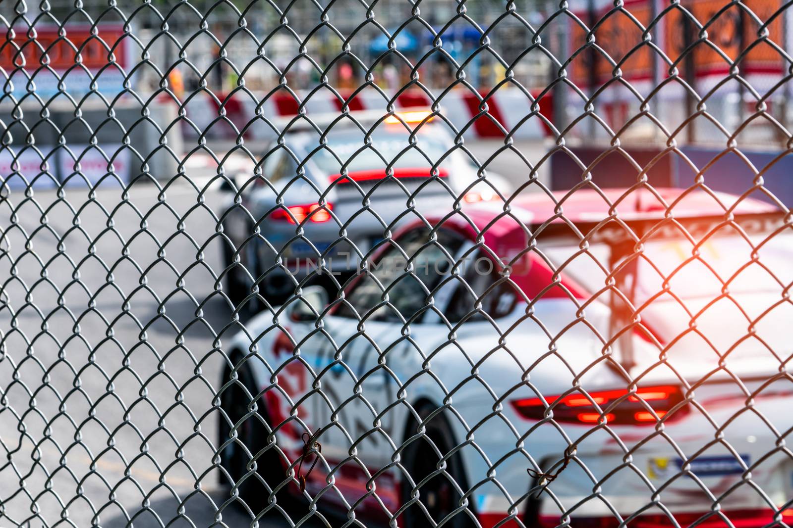 Motorsport car racing on asphalt road. View from the fence mesh netting on blurred car on racetrack background. Super racing car on street circuit. Automotive industry concept. by Fahroni