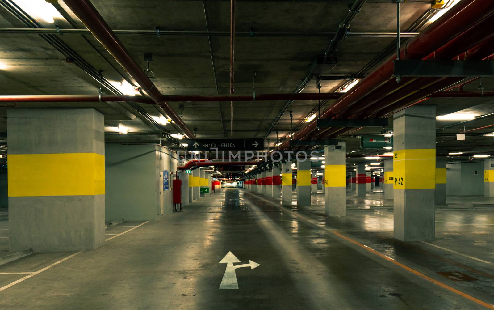 Perspective view of empty indoor car parking lot at the mall. Underground concrete parking garage with open lamp at night. White direction sign. Choose way to live your life. Wiring and plumbing. by Fahroni