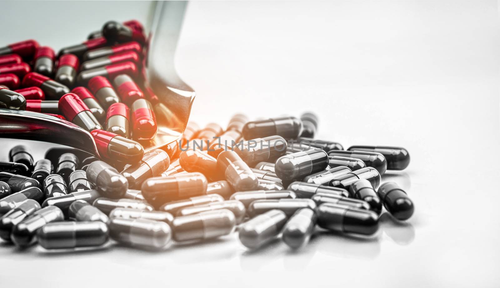 Red and grey capsule pills on stainless steel drug tray and gray capsules on white background. Migraine prophylaxis treatment concept. Global healthcare concept. Pharmaceutical industry. by Fahroni